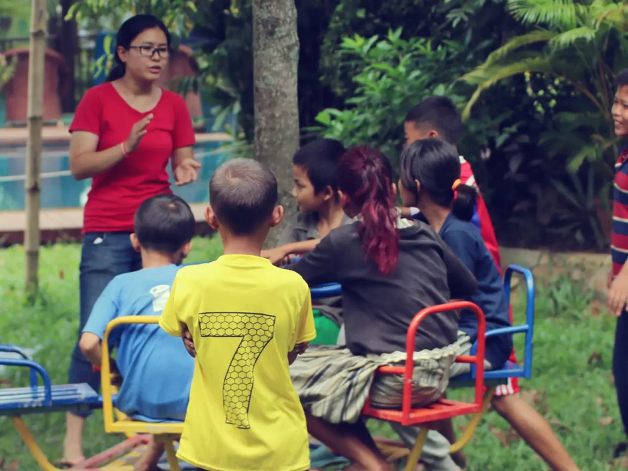 In the foreground of the picture, there are girls and boys are on a merry go round park equipment....